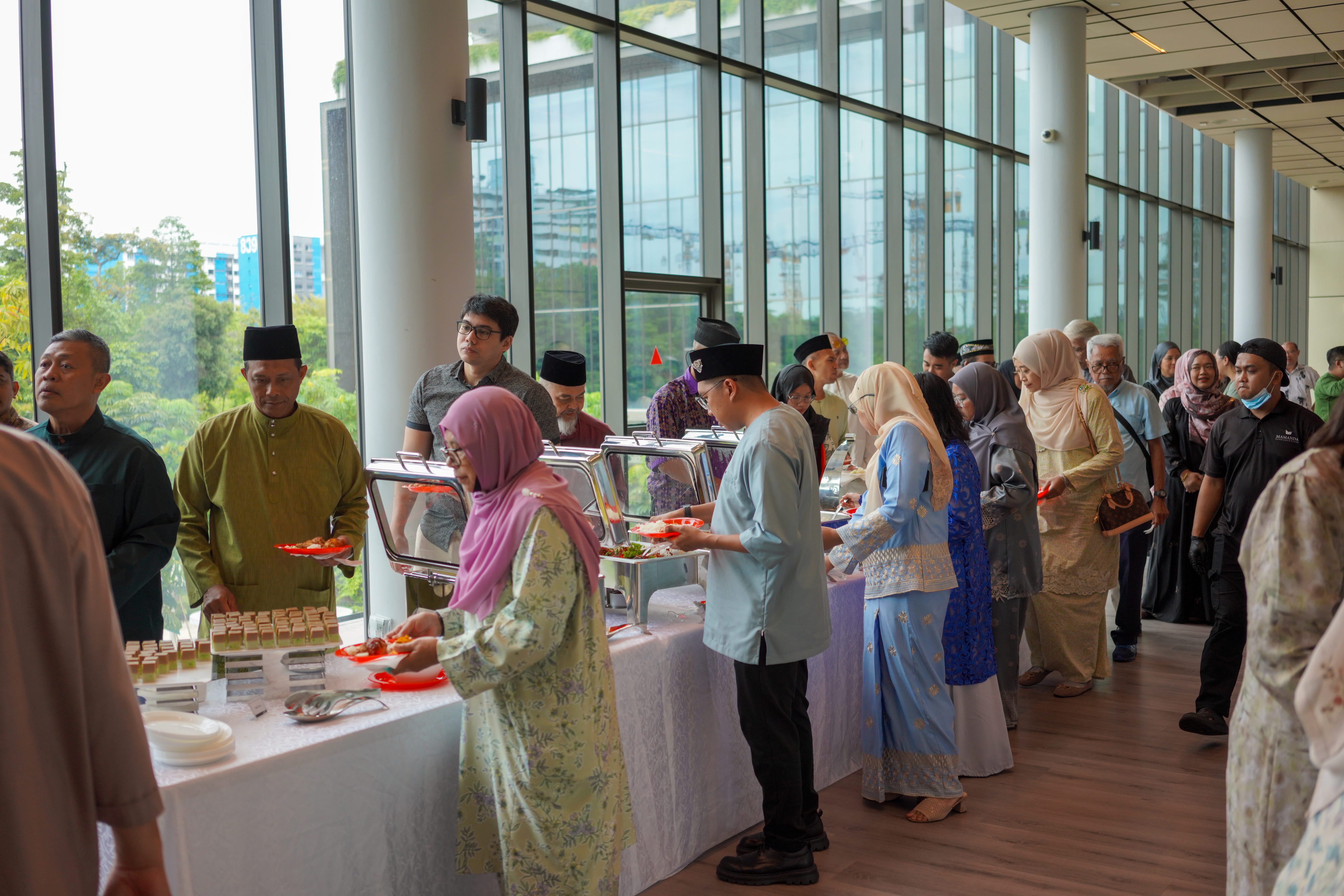 Attendees queueing at a buffet line beside floor-to-ceiling windows while selecting food.